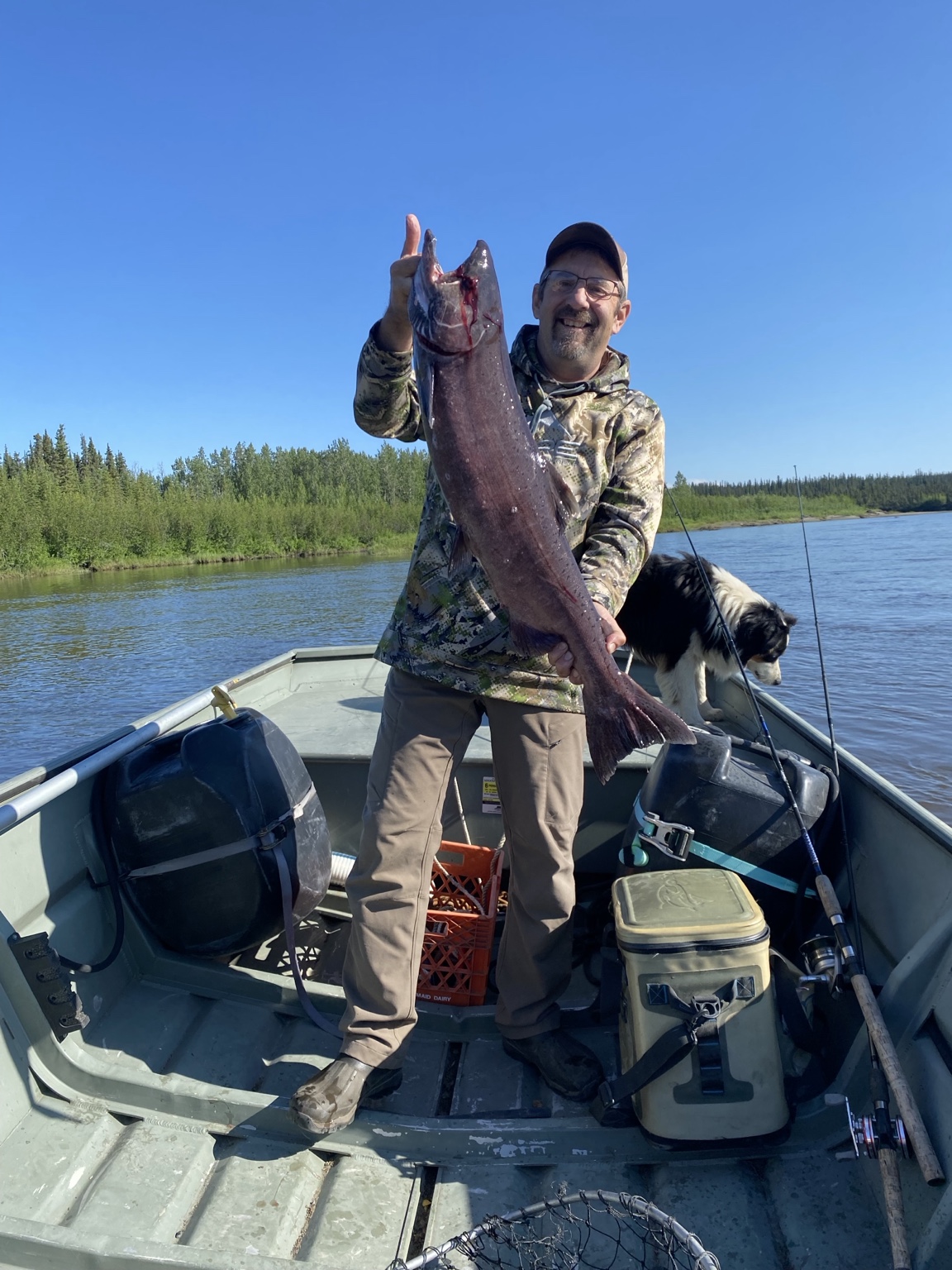 Tom Anderson holding a king salmon in a riverboat with his dog