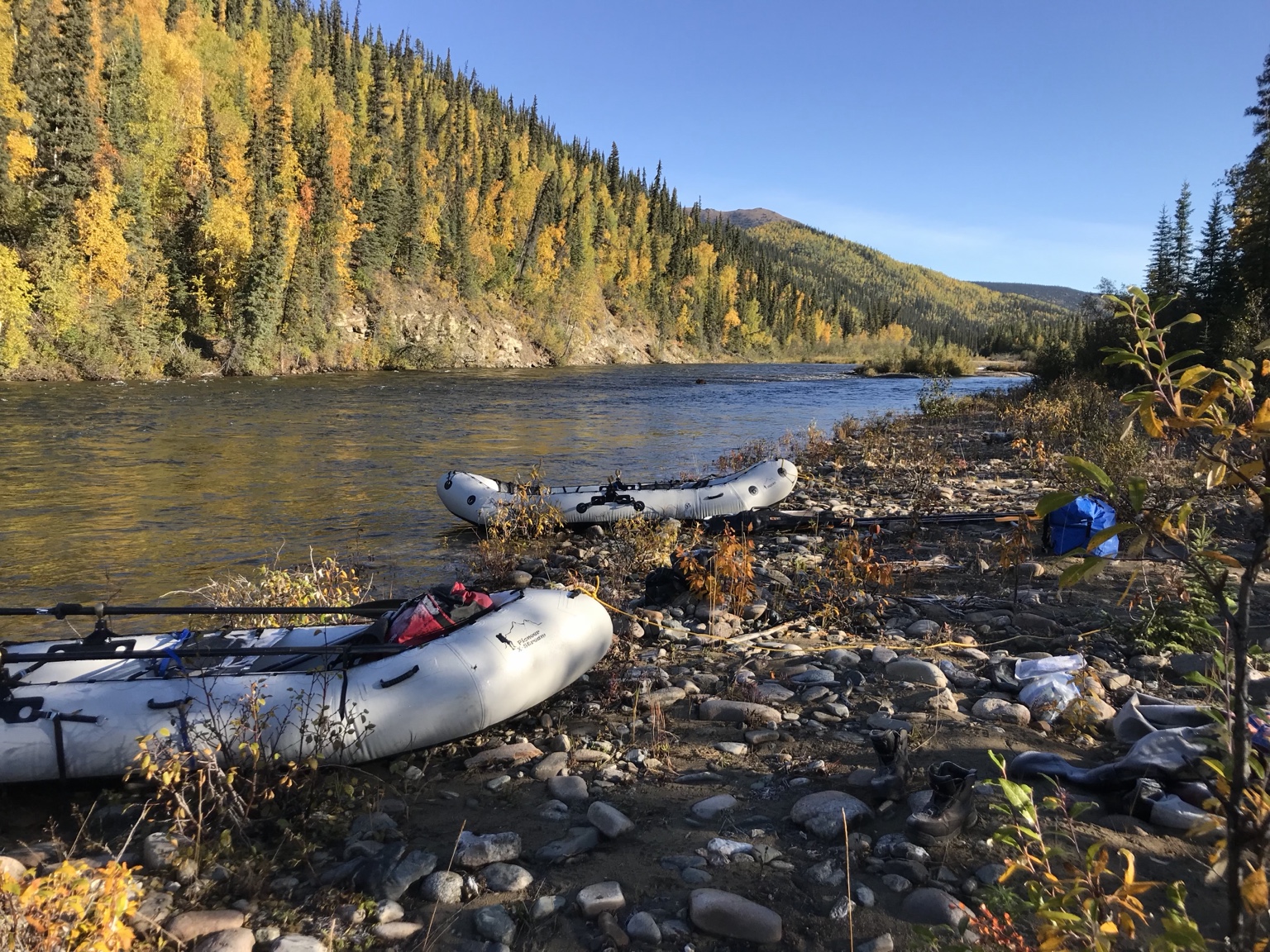 Custom-rigged inflatable boats on a rocky Alaskan riverbank with fall-colored hills